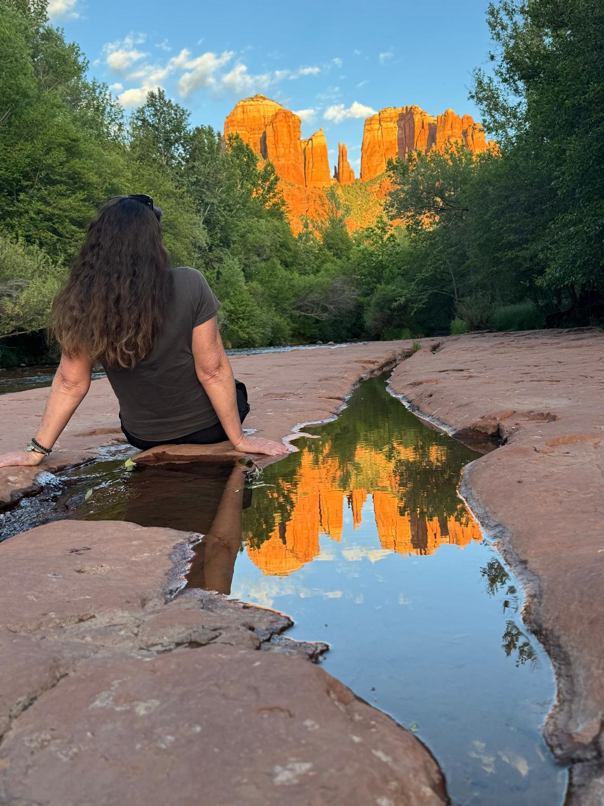 Jennifer Spencer sitting on the rock at Cathedral Rock, looking at the red cliffs reflected in the water
