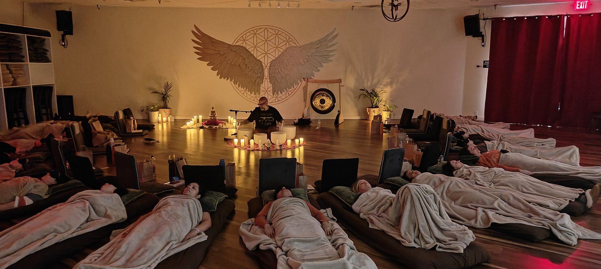 Steve Fernandez playing singing bowls while the group lies wrapped in blankets around him, lit by candles